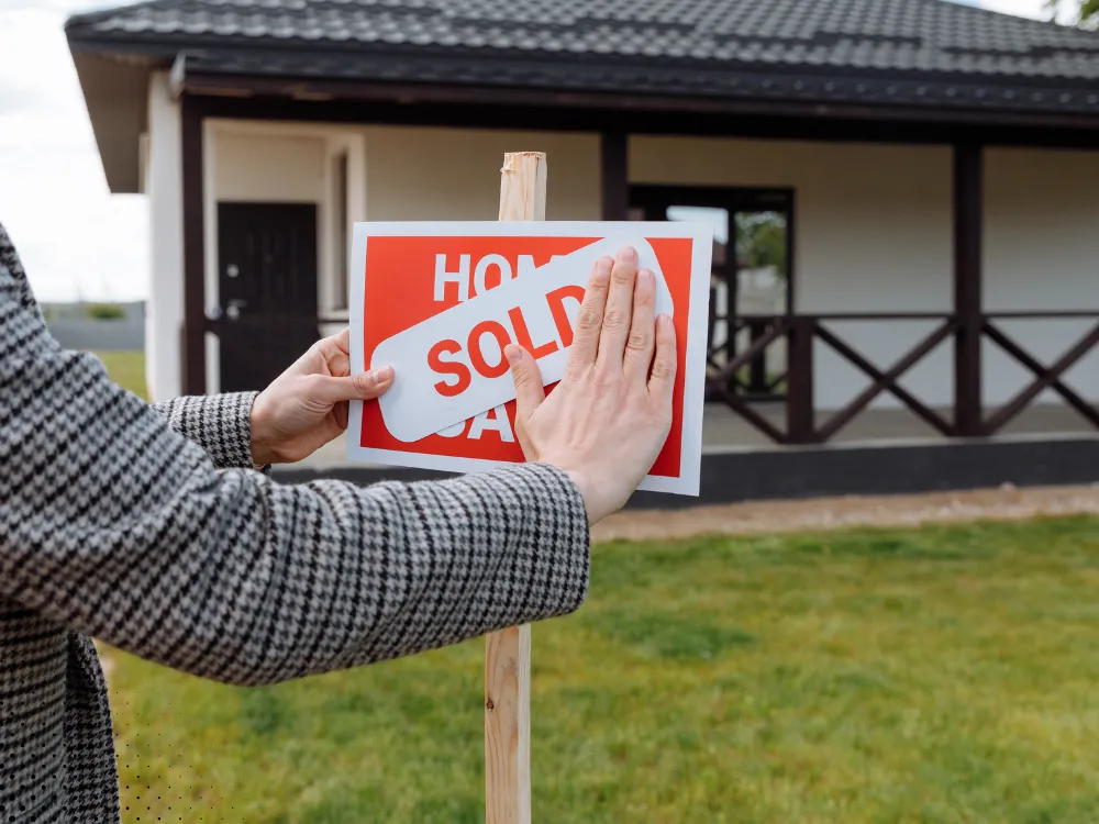 Home seller placing a 'SOLD' sticker on a property sign, marking the successful sale of a home after inspection