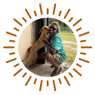 A warm, hopeful photo of a healthy dog in a remote community receiving care from a smiling volunteer