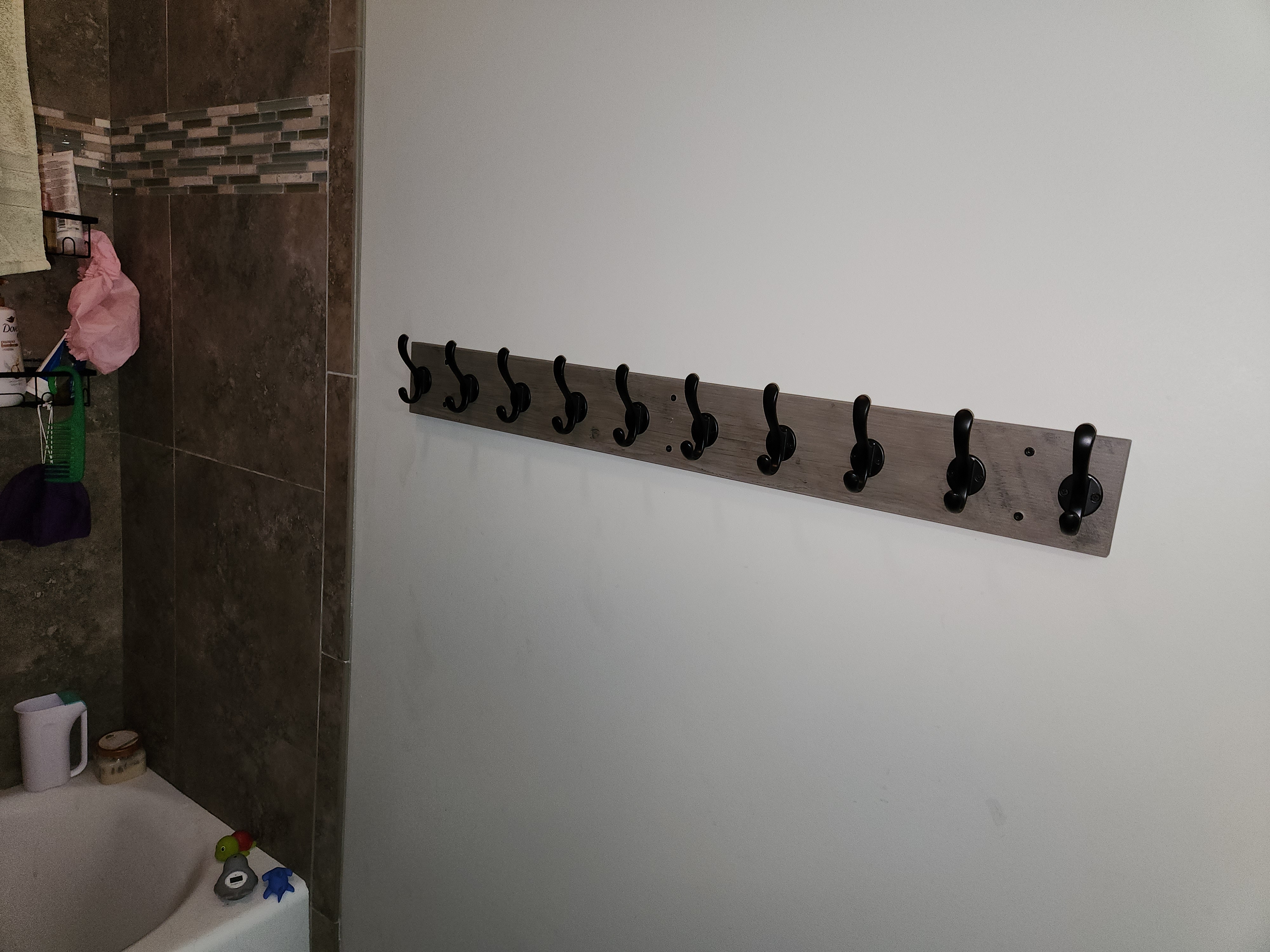 Wood wall rail with black coat hooks installed in a home