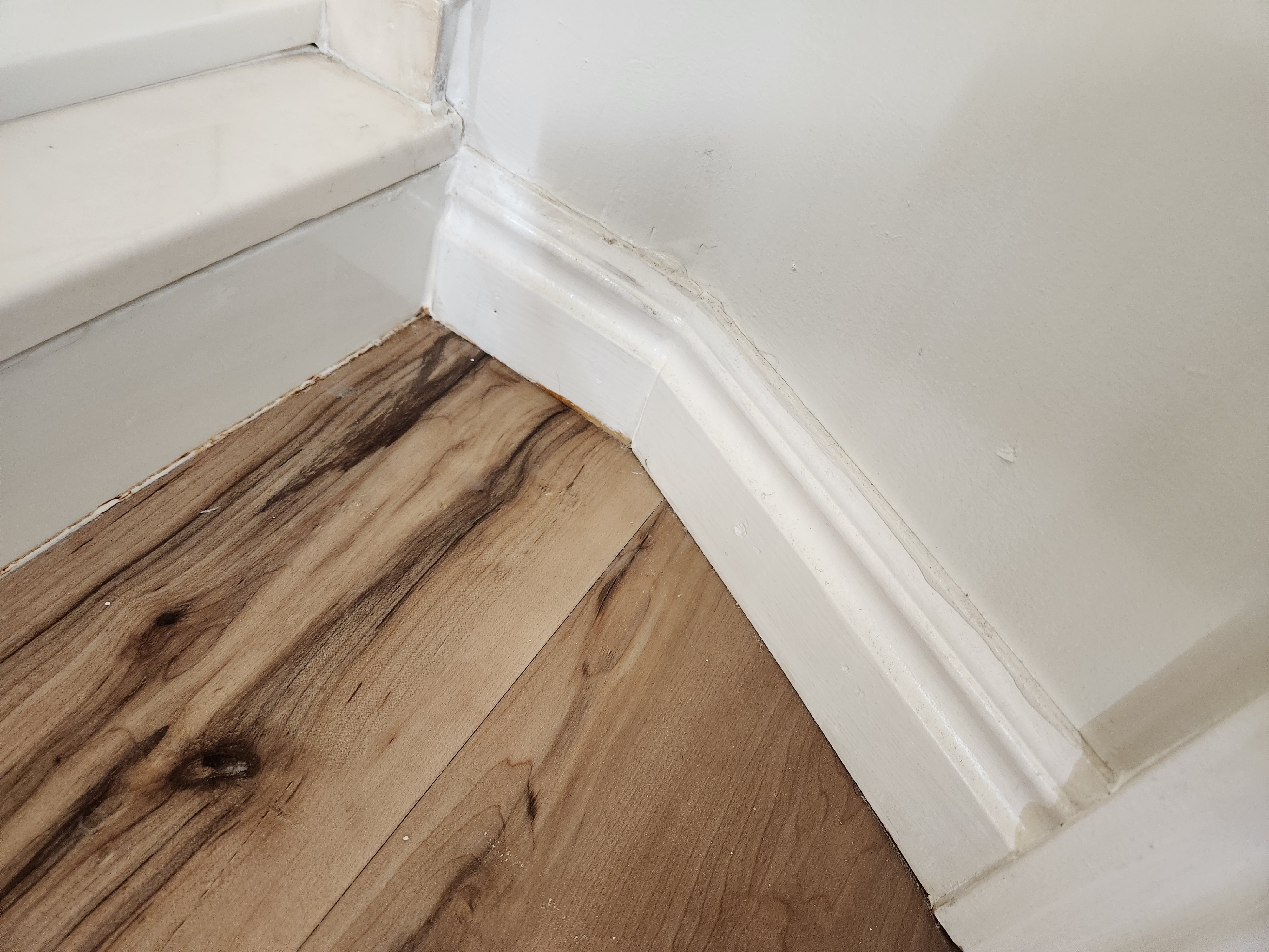 Finished white baseboard trim around an interior corner