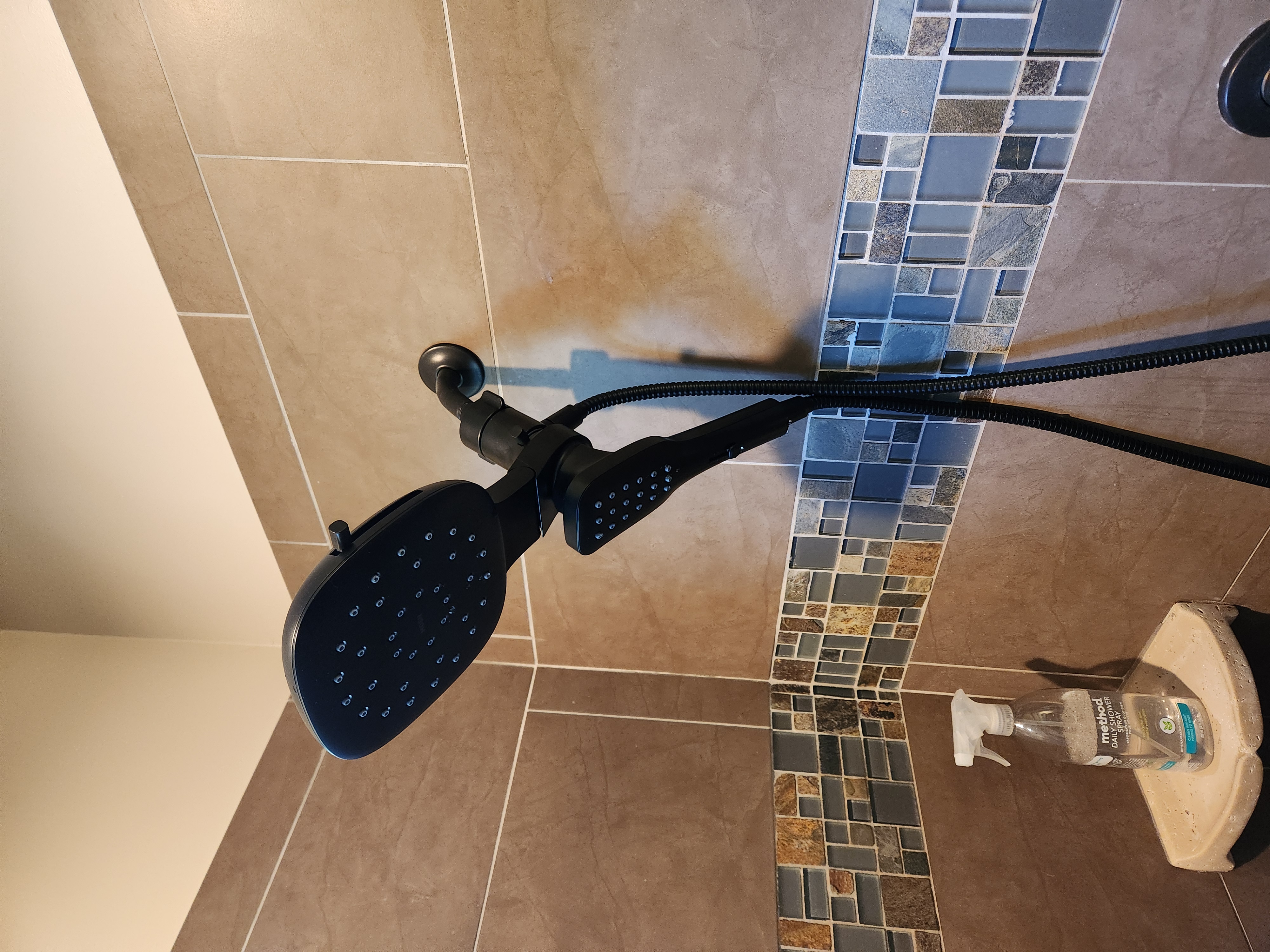 Black showerhead and handheld fixture in a tiled shower