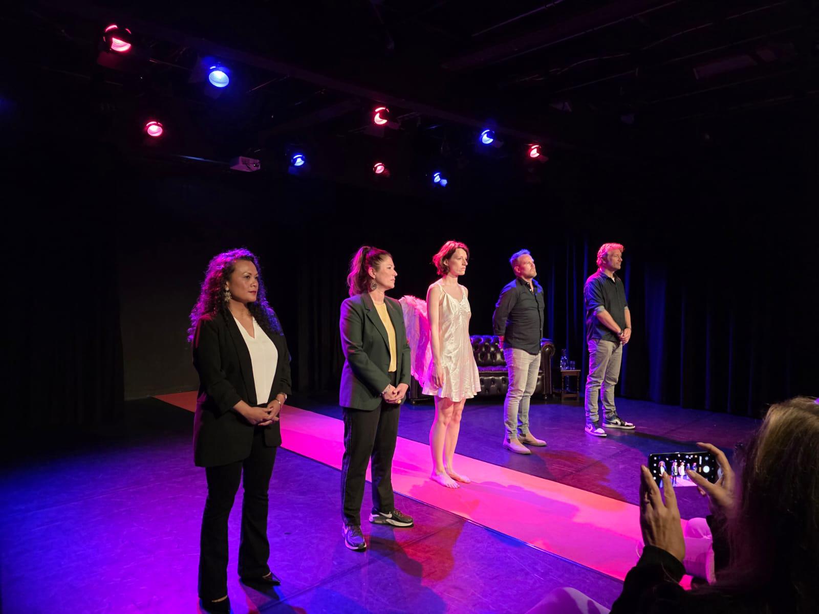 Een vrouwelijke instructeur die traumazorgconcepten presenteert op een digitaal scherm aan een aandachtig publiek in een moderne collegezaal. De omgeving is helder, met zachte neutrale verlopen en een minimalistische inrichting, wat vernieuwing en leren benadrukt.