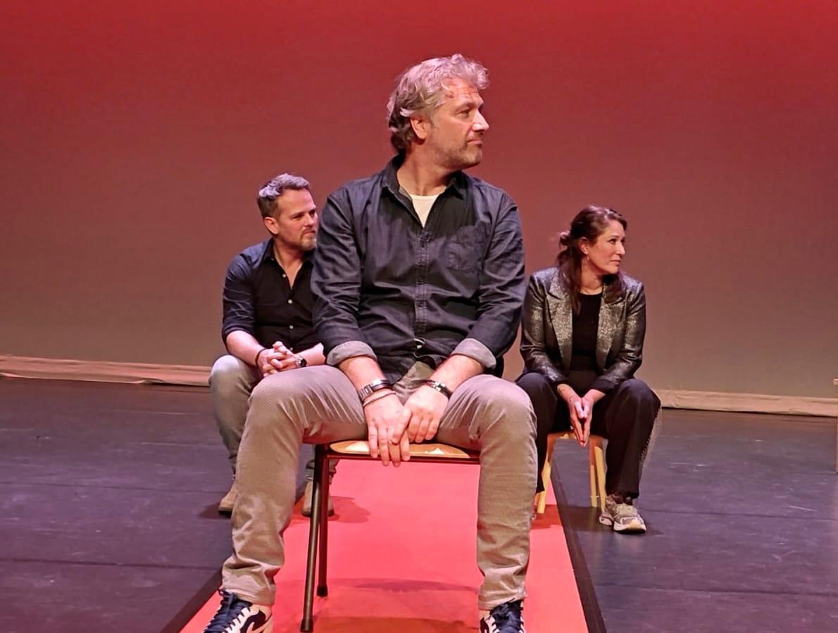 Een vrouwelijke instructeur die traumazorgconcepten presenteert op een digitaal scherm aan een aandachtig publiek in een moderne collegezaal. De omgeving is helder, met zachte neutrale verlopen en een minimalistische inrichting, wat vernieuwing en leren benadrukt.