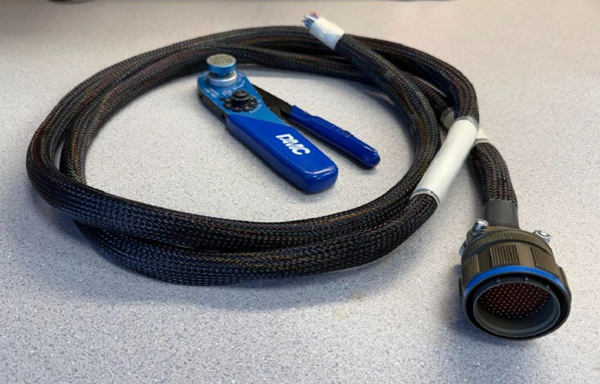 Close-up of mil-spec aircraft wiring harness construction with shielding termination, backshell strain relief, and labeled wire bundle dressing.
