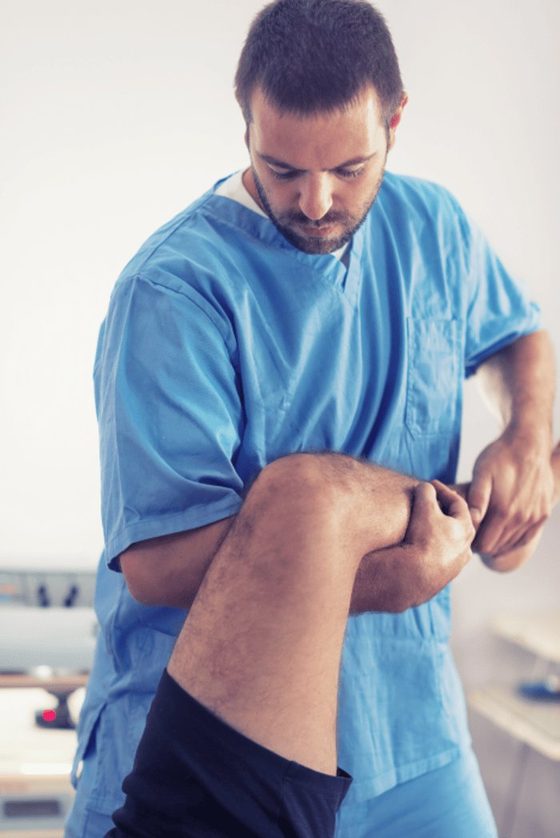 Male chiropractor in blue scrubs standing and examining notes or charts.