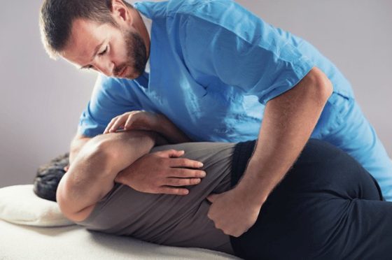 Chiropractor performing a mid-back adjustment on a male patient lying face down on a treatment table.