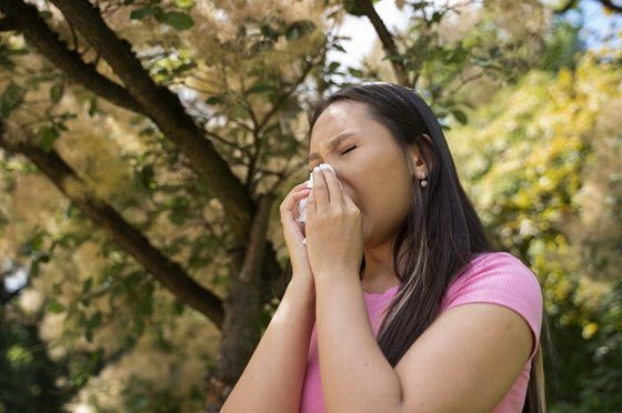 Woman holding a tissue to her nose outdoors, appearing to have allergies