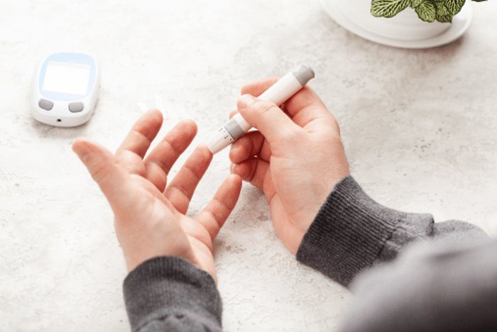 Close-up of a person's hands using a blood glucose meter, pricking a finger.