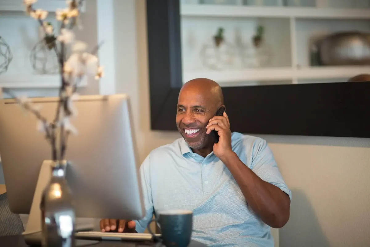 Happy Male Business Owner on his cell phone will looking a his iMAc Screen