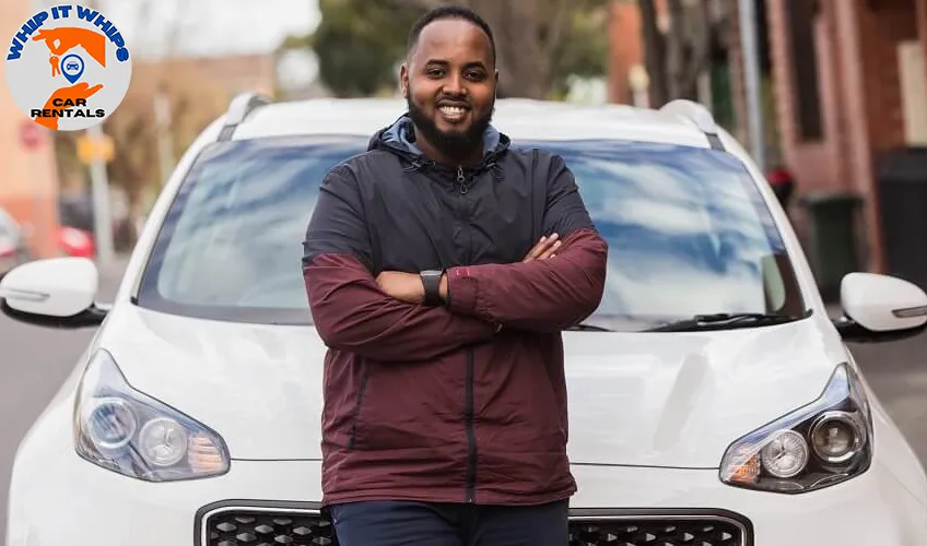 Professional portrait: The image features a smiling man standing in front of a white car, posing for a picture.