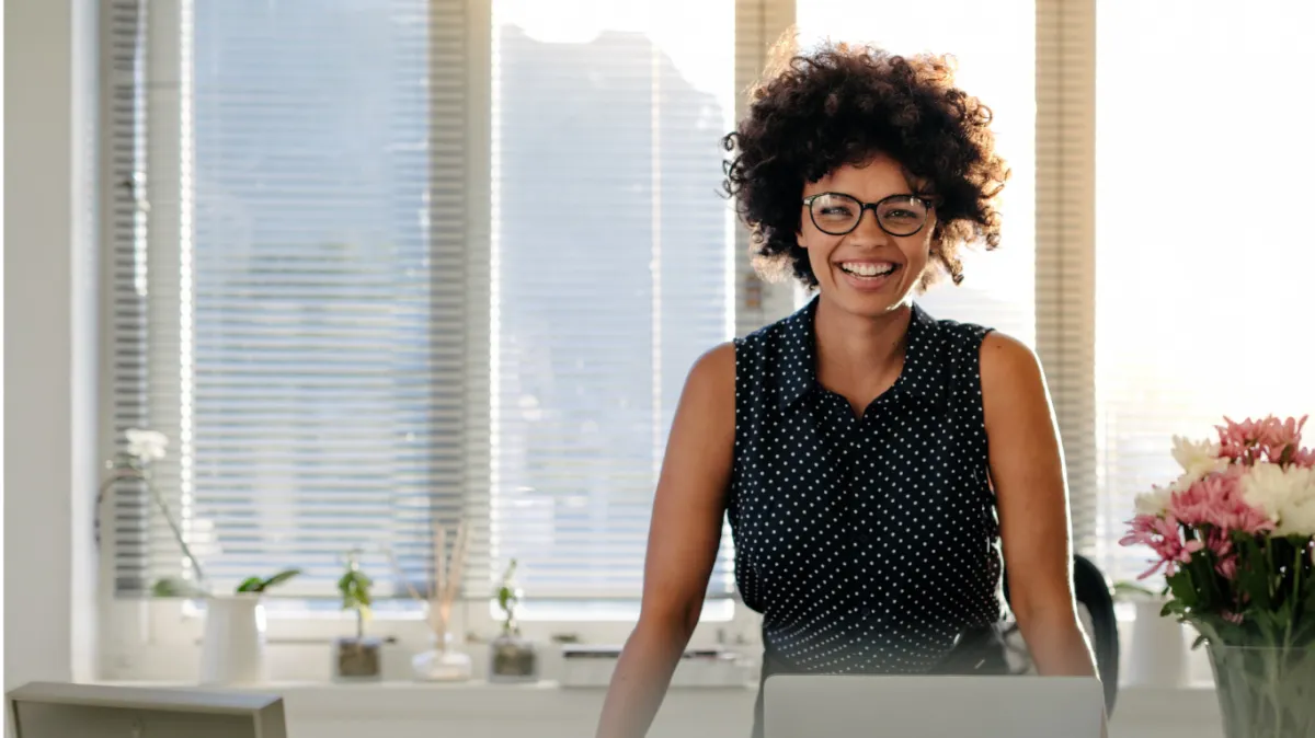 woman looking frustrated with hands on her face and eyes closed, sitting at a desk with latop and papers on it