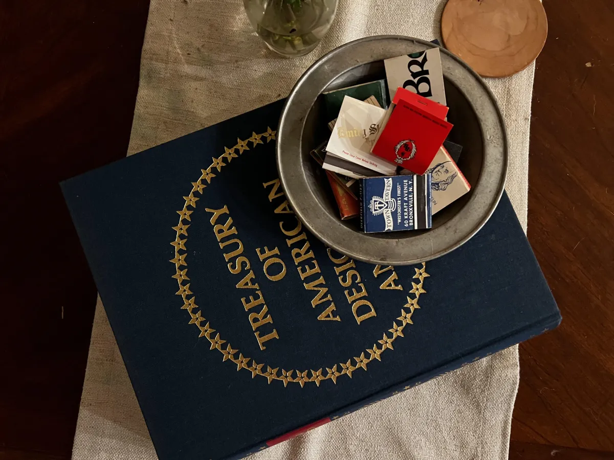 The Manor's elegantly arranged coffee table showcasing 'The Treasury of American Design' encyclopedia and a collection of unique, artistically designed matchboxes, reflecting our focus on rare and interesting decor.