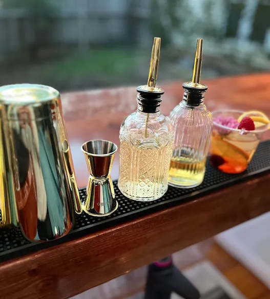 Elegant mobile bar setup from the Ratlin Package featuring gold bar tools, crystal syrup bottles, and a fresh fruit garnish, captured from behind the bar at a San Antonio event