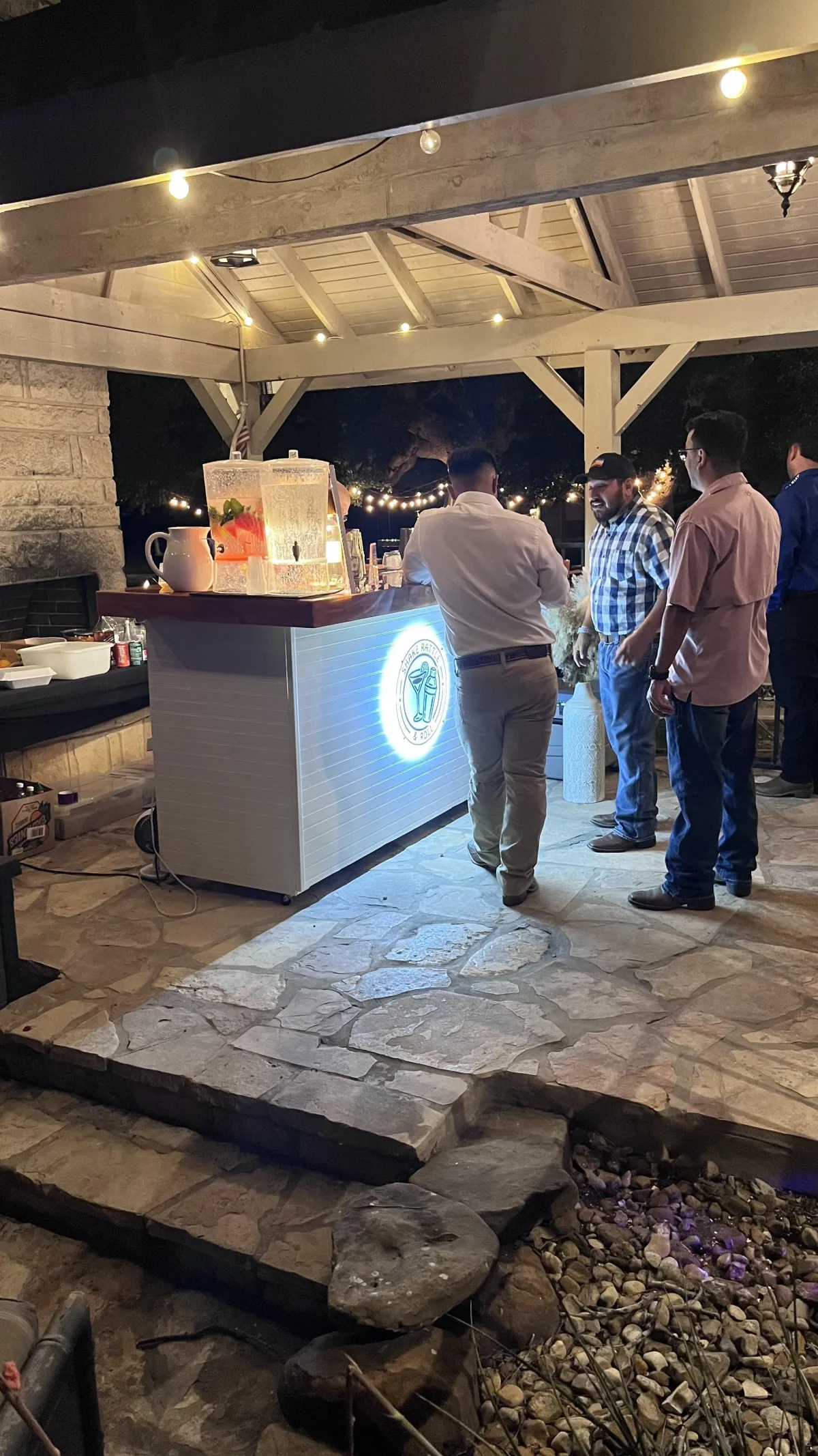 Guests enjoying an evening private party in San Antonio with Shake Rattle & Roll’s illuminated mobile bar and professional bartender service under a covered patio.