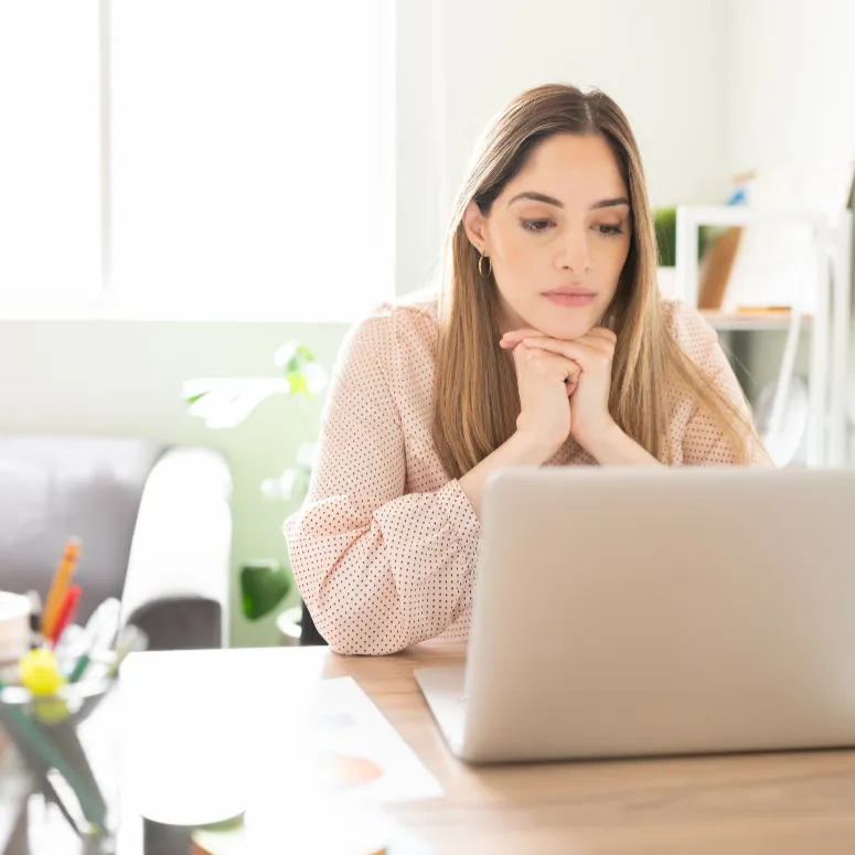 Blonde woman looking at her laptop open on her desk in home office.