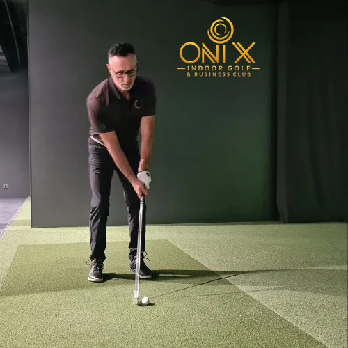 Golfer teeing off inside Onix private luxury indoor simulator bay with moody gold ambient lighting