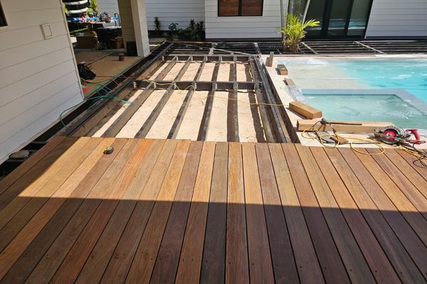 Close-up of composite decking, stainless steel fasteners, and weatherproof finishes, arranged on a workbench with tropical foliage in the background.