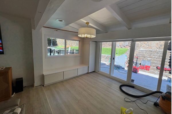 A bright, modern kitchen renovation in a Hawaiian home, featuring open shelving, koa wood accents, and large windows with tropical foliage visible outside, demonstrating a blend of local materials and contemporary design.