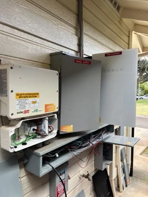 A close-up of a digital solar inverter display showing a red error warning, with a concerned homeowner and a technician in the background. The setting is a Hawaiian home interior, sunlight streaming through windows, conveying urgency and the need for immediate solar repair.