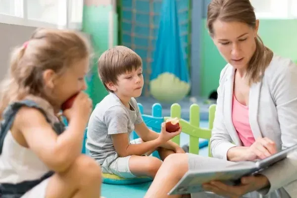 A young girl intently paints colorful strokes on paper using a brush and multiple paint jars around her.