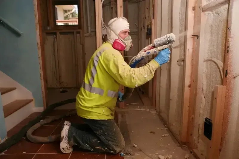 Technician applying open-cell spray foam to wall cavity in Raleigh home for energy savings and soundproofing