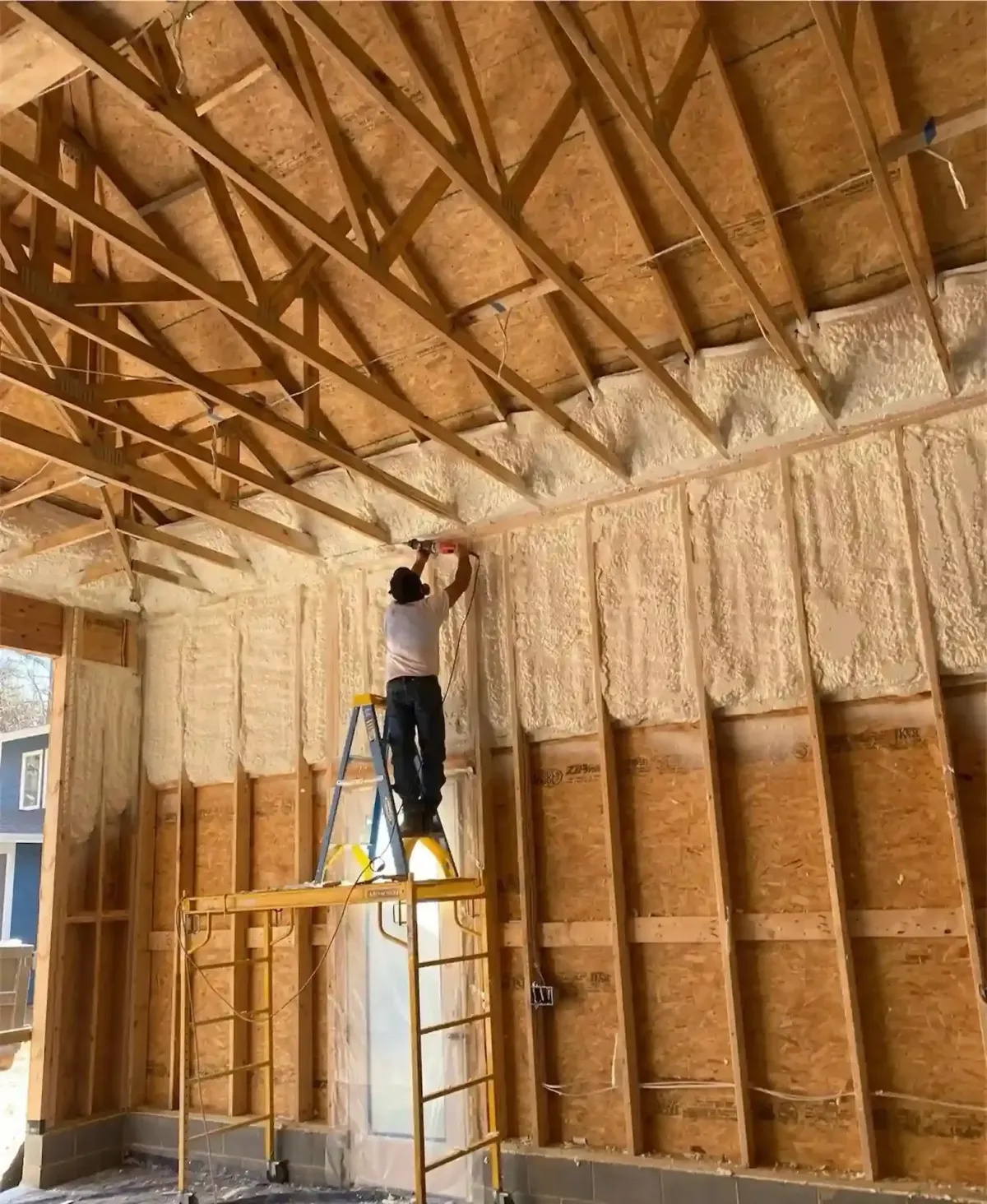 Contractor installing fiberglass or blown-in insulation in high walls of a new build in Clayton, NC to improve energy efficiency