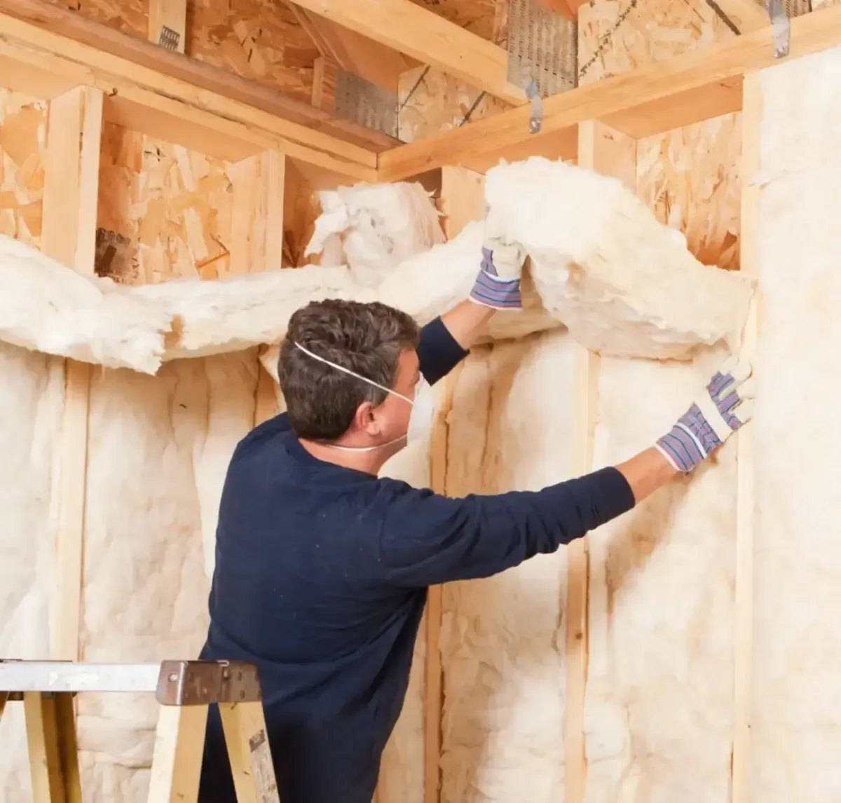 Installer placing fiberglass batt insulation in wall framing in Fuquay-Varina attic
