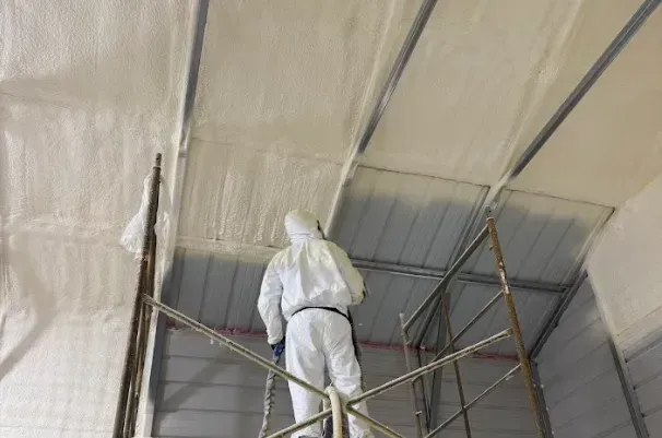 Professional installer applying open-cell spray foam insulation to a building ceiling for Energy Saving Insulation in the Triangle area