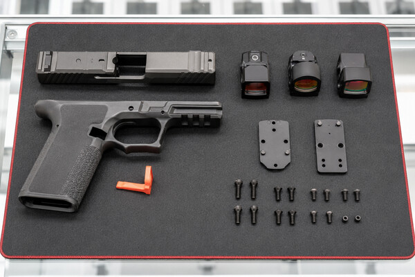 An optic-ready handgun with several red-dot sights, adapter plates, and mounting screws arranged on a work mat.