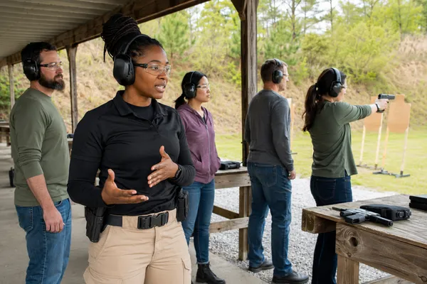 Female firearms instructor leading a diverse group of adults at an outdoor shooting range