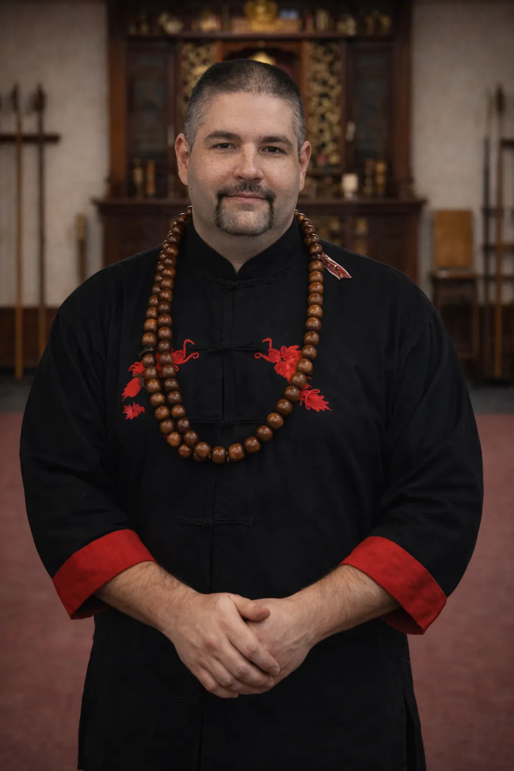 Portrait of Grandmaster David Harris in a black and red uniform wearing traditional meditation beads in a martial arts dojo setting.