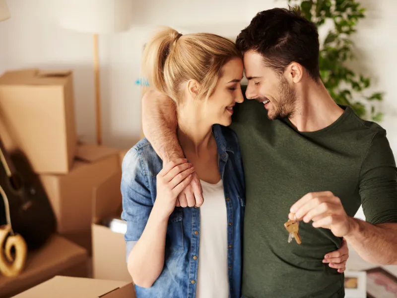 Happy couple embracing and holding house keys in their new home after closing on a mortgage.