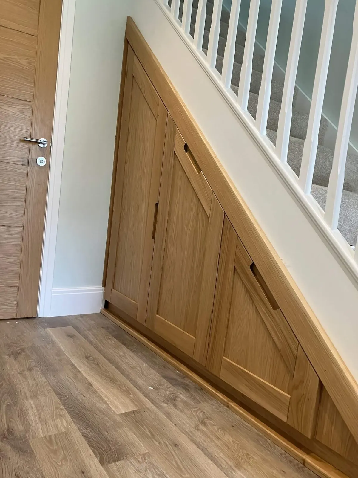 Bespoke oak under-stairs storage unit with angled doors and integrated handles, oak door finish