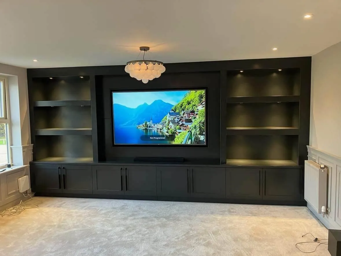 Black furniture style media wall unit with illuminated shelving and base cabinets, featuring mounted TV