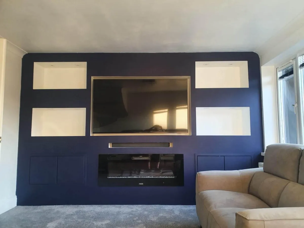 Navy blue media wall with electric fire, soundbar, and decorative alcoves, featuring LED lit TV mount