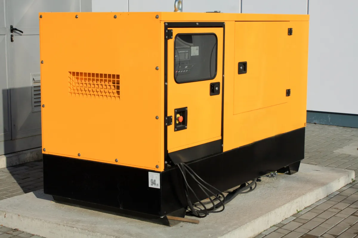 Bright yellow industrial backup generator placed on a concrete pad outside a building, equipped with control panel and power cables for emergency energy support.
