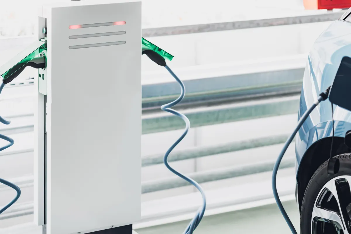 Close-up of a white dual-port EV charging station with blue charging cables connected to two electric vehicles inside a modern parking garage.