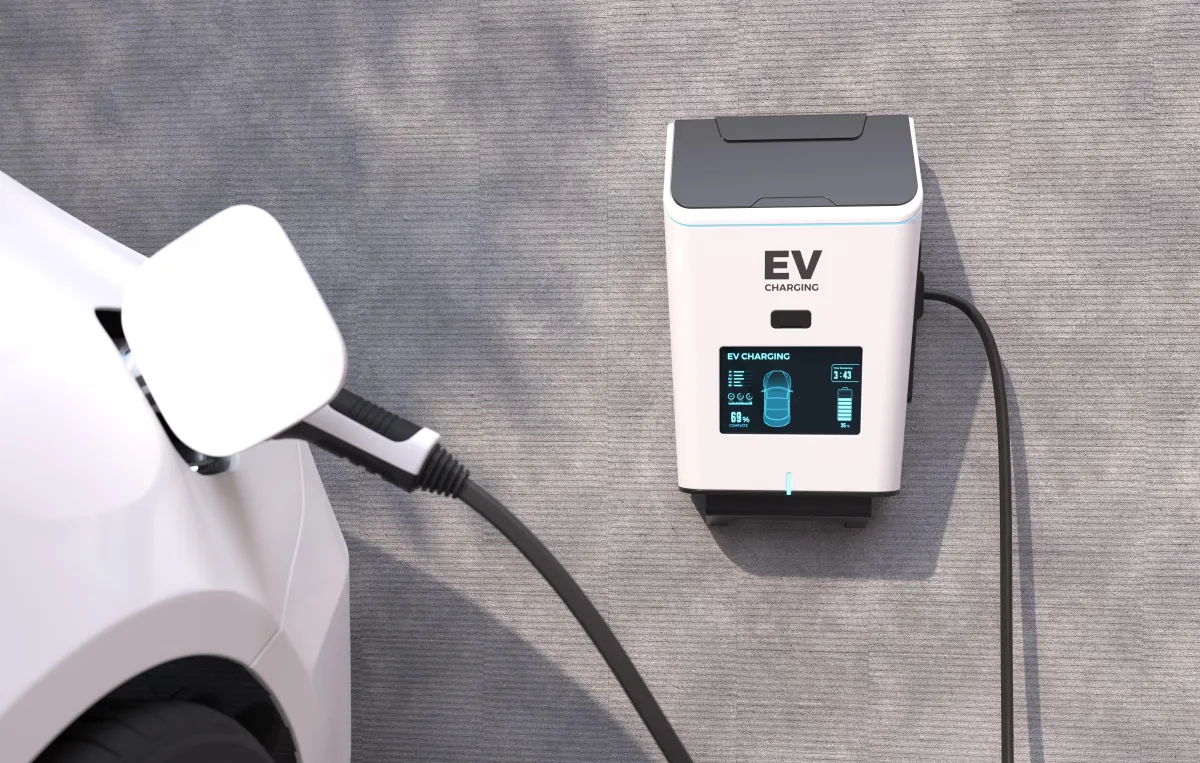 Electric vehicle charging from a sleek wall-mounted EV charger with digital display, connected to a white car parked alongside a concrete wall.