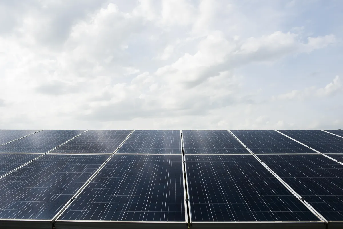 Wide view of solar panels under a partly cloudy sky, capturing clean energy from sunlight as part of a ground-mounted or rooftop solar installation.
