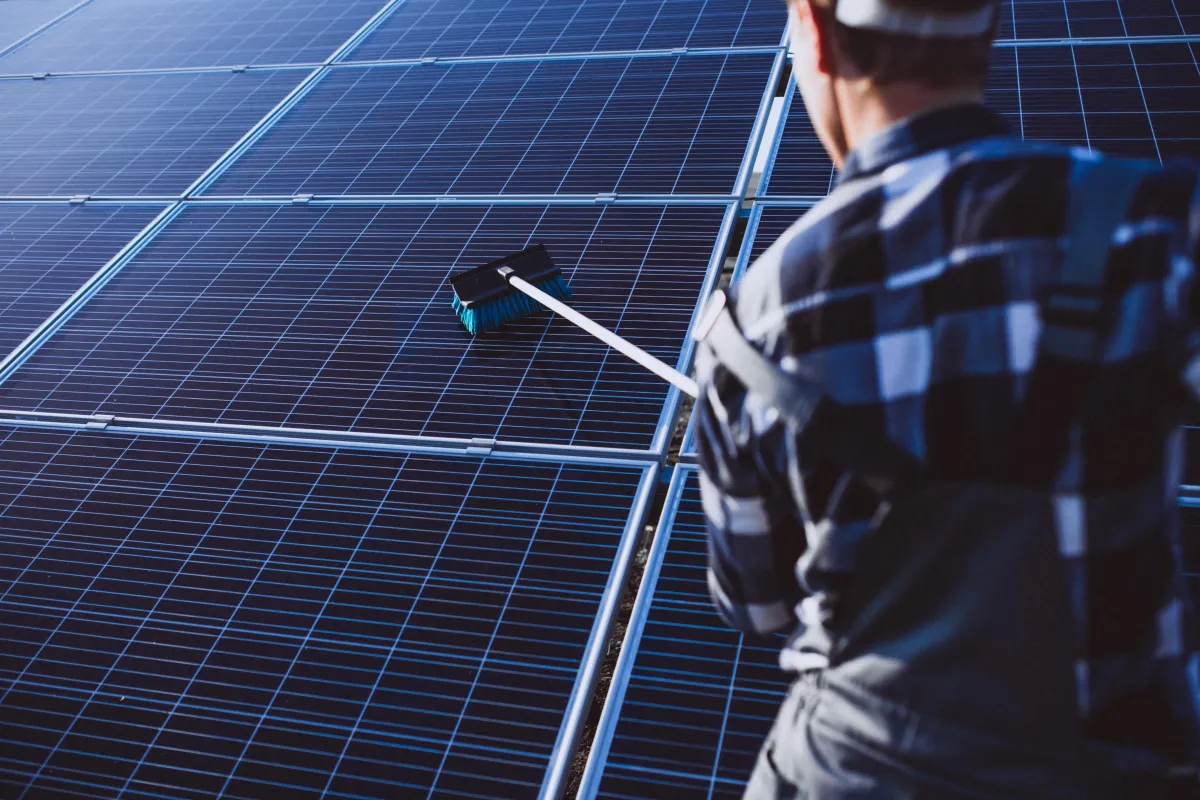 Technician using a long-handled brush to clean large solar panels, ensuring optimal performance and energy efficiency during solar panel maintenance.