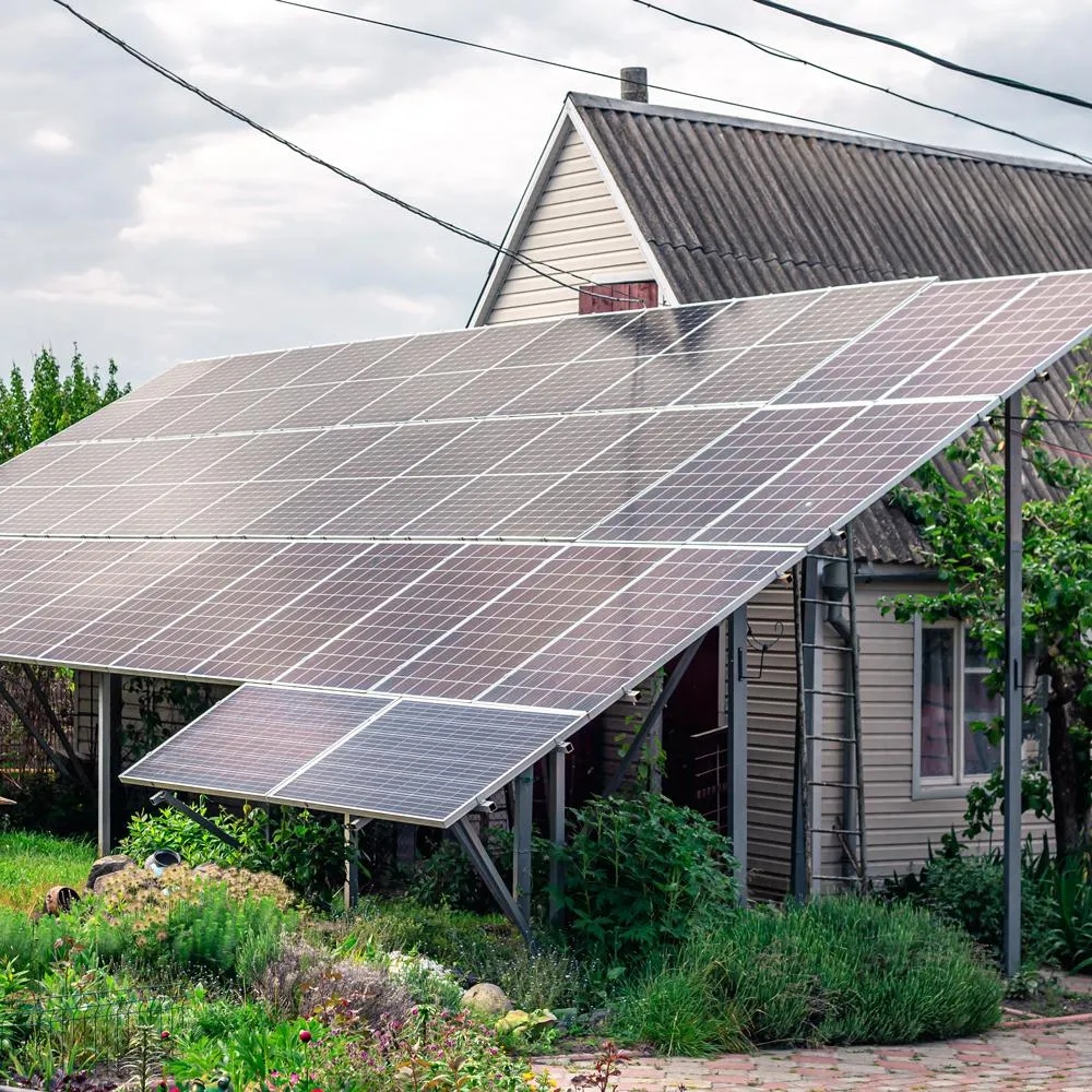 Ground-mounted solar panel array installed on a steel frame in front of a residential home, providing both energy generation and partial shading over a garden area.