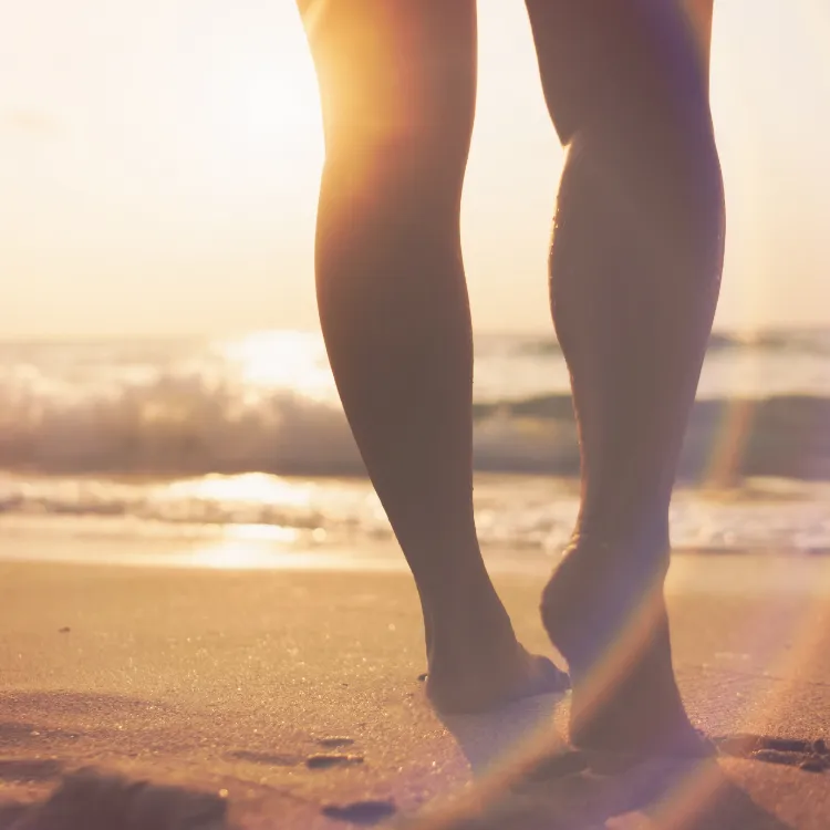 Barefoot woman standing in nature with sunlight through leaves, reflecting ecological connection, balance, and whole-body wellness.