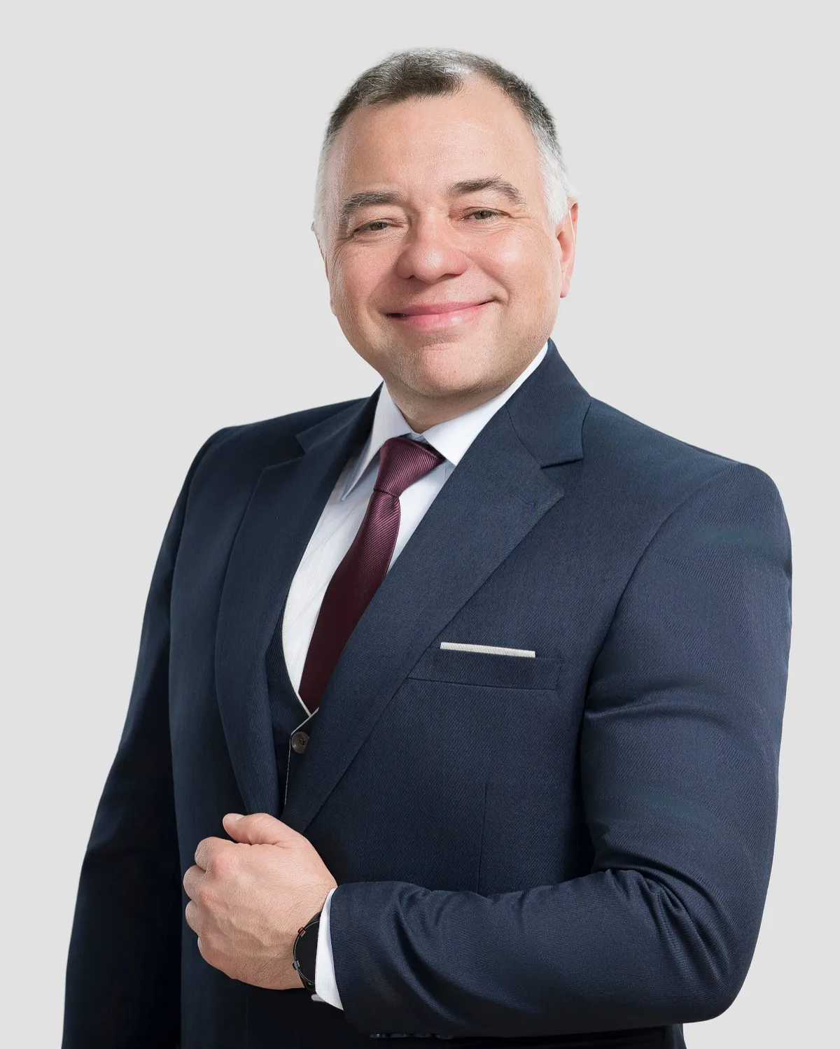 Portrait of the man in a dark suit, white shirt, and burgundy tie, smiling