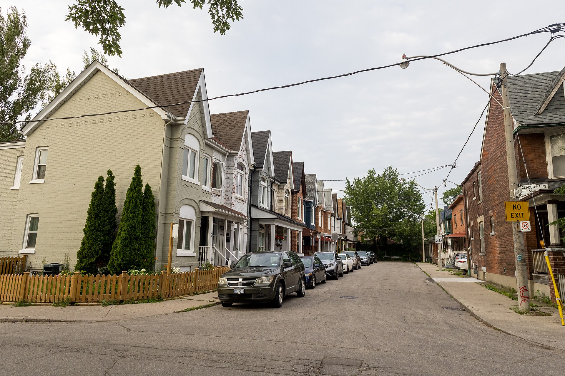Row of narrow gabled semi detached and row houses with front porches along Langemark Avenue in Little Portugal, Toronto