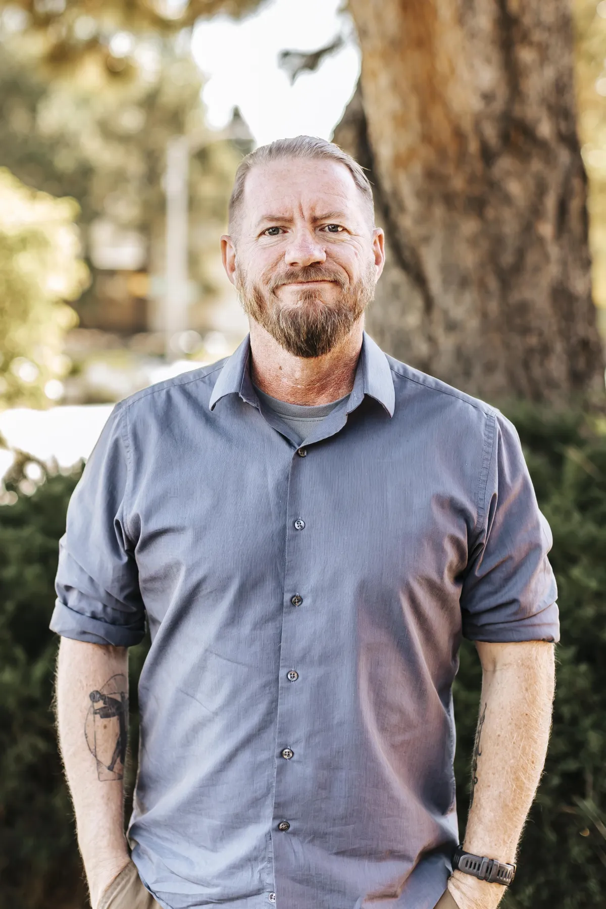 Man with a beard wearing a blue button-up shirt, standing outdoors in front of greenery, representing expertise in technology and software development for Revflow Growth Partners.