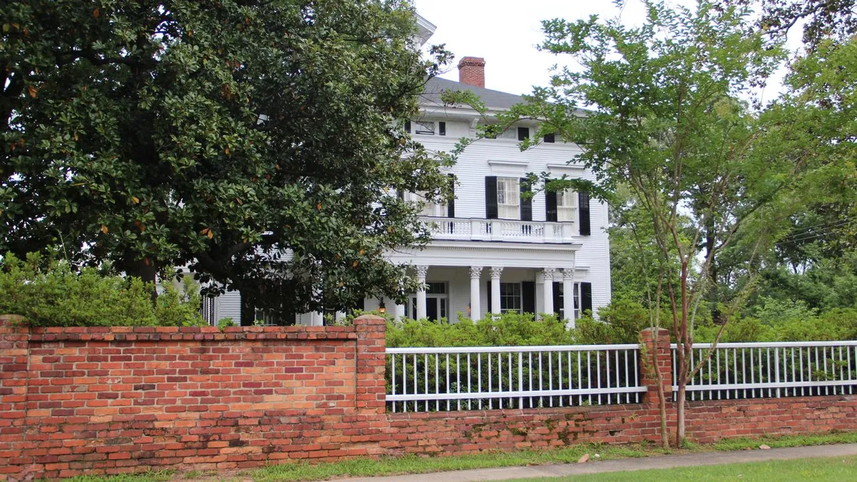 White two-story historic home with columns behind a brick wall and magnolia tree in the Summerville neighborhood of Augusta, GA