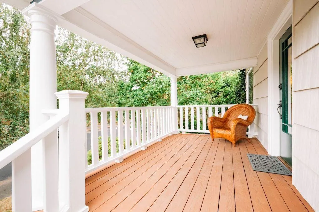 Deck with freshly stained wood, white railing, and wicker chair, surrounded by greenery, showcasing the quality of Copeland Painting's deck staining services in Paducah, KY.