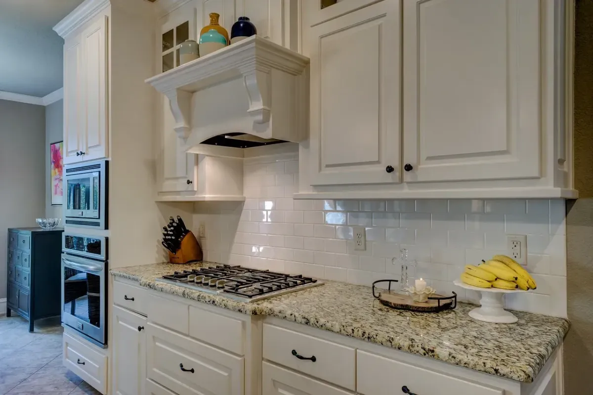 Modern kitchen with white cabinetry, granite countertop, stainless steel appliances, and decorative items including a bowl of bananas and a candle, showcasing Copeland Painting's cabinet painting services for a refreshed look.