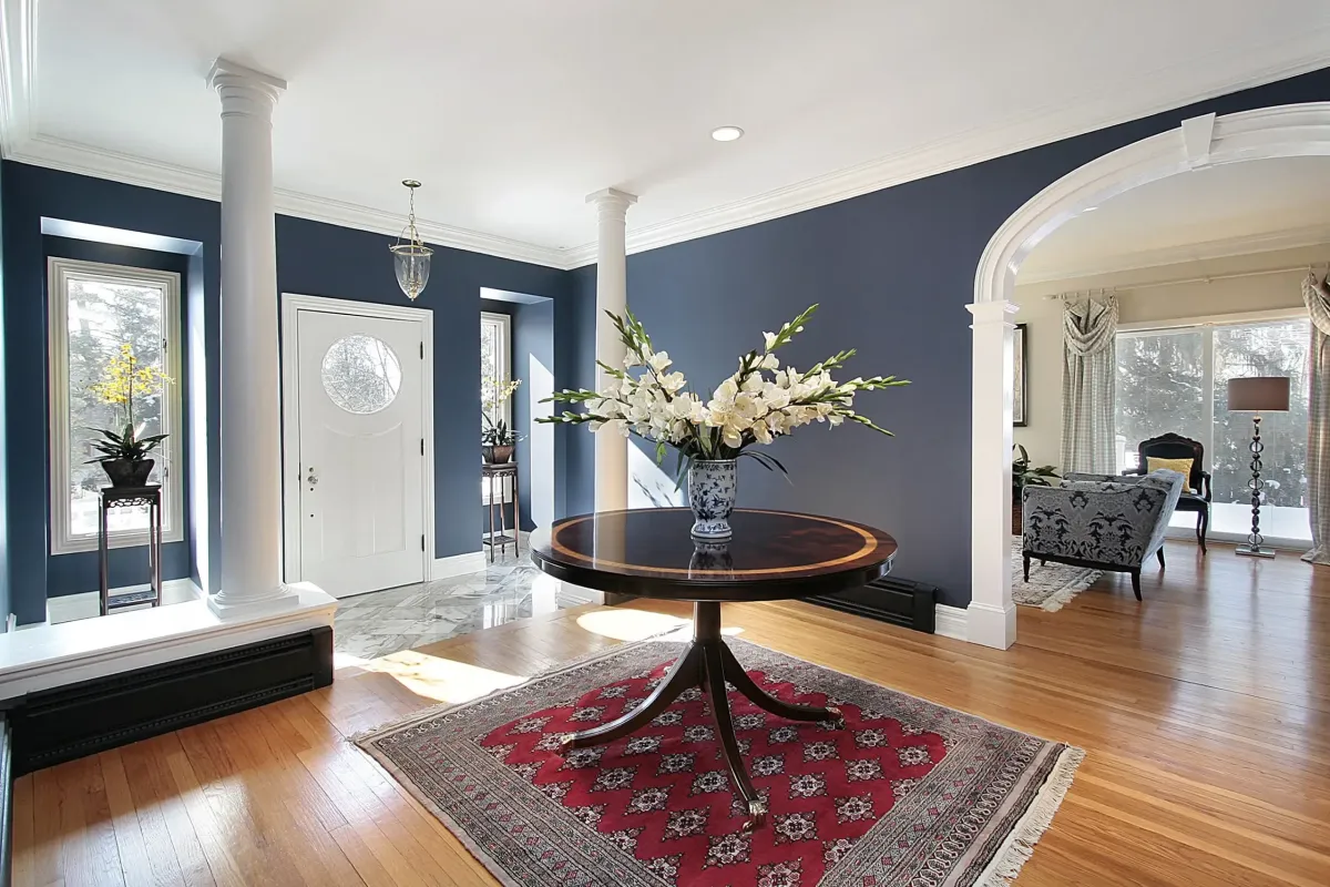 Elegant interior entryway with dark blue walls, a round wooden table topped with white flowers, and marble flooring, showcasing a stylish home transformation by Copeland Painting in Paducah, KY.