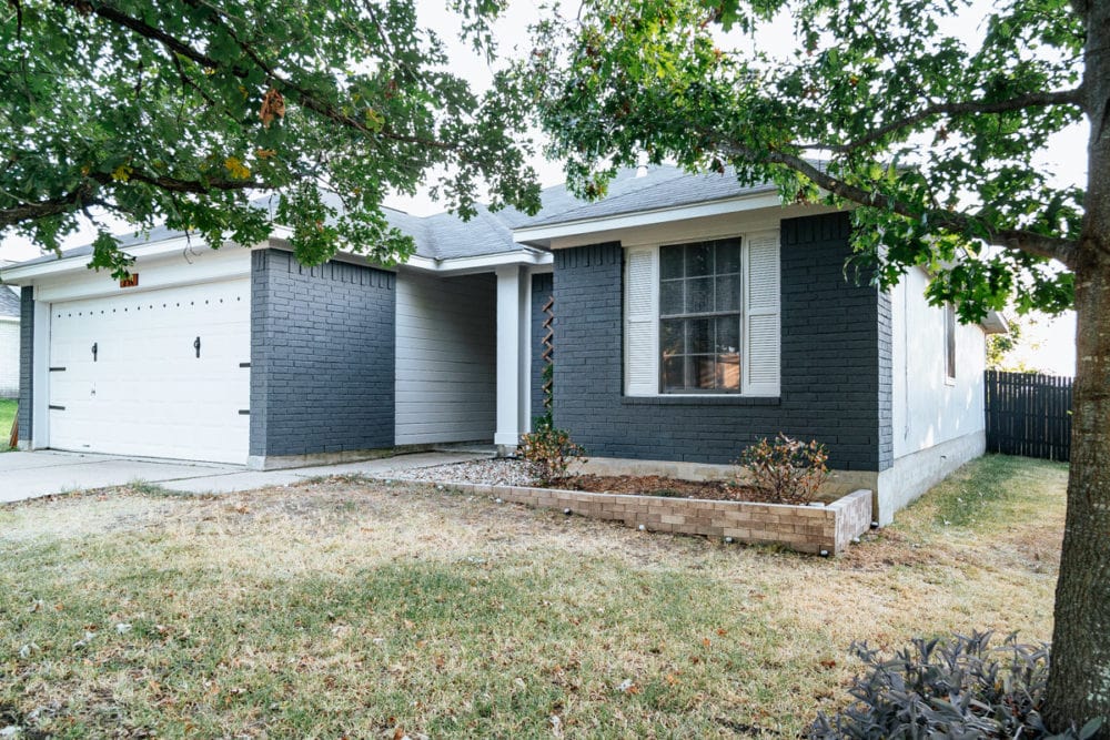 Exterior view of a recently painted home in Mayfield, KY, showcasing dark gray brick and light gray siding, with a well-maintained yard and garage, emphasizing professional exterior painting services.
